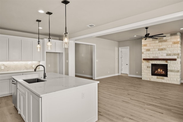 kitchen with a kitchen island with sink, white cabinets, sink, ceiling fan, and light stone counters