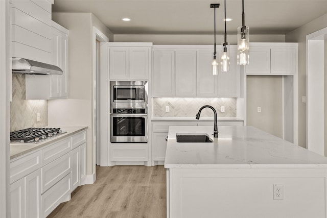 kitchen with sink, wall chimney exhaust hood, decorative light fixtures, a kitchen island with sink, and appliances with stainless steel finishes