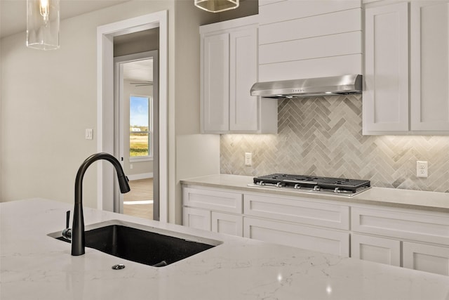 kitchen featuring sink, stainless steel gas cooktop, light stone counters, pendant lighting, and extractor fan