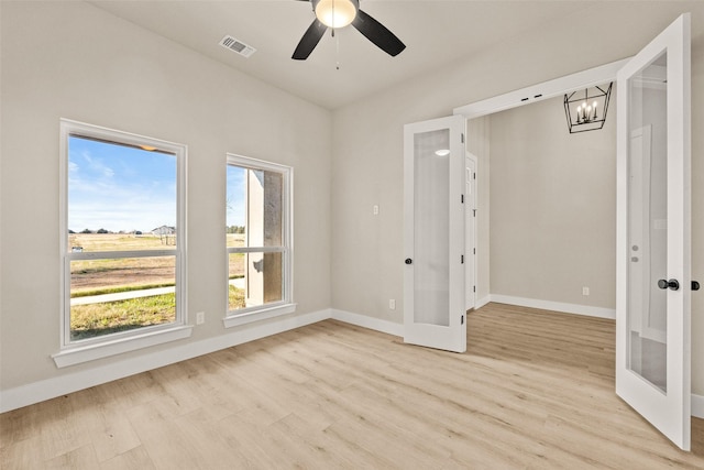 spare room featuring french doors, ceiling fan with notable chandelier, and light wood-type flooring