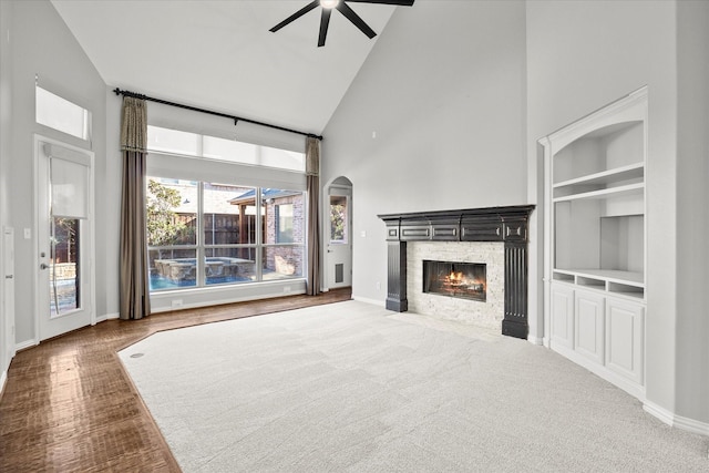 unfurnished living room with ceiling fan, a stone fireplace, high vaulted ceiling, and built in shelves