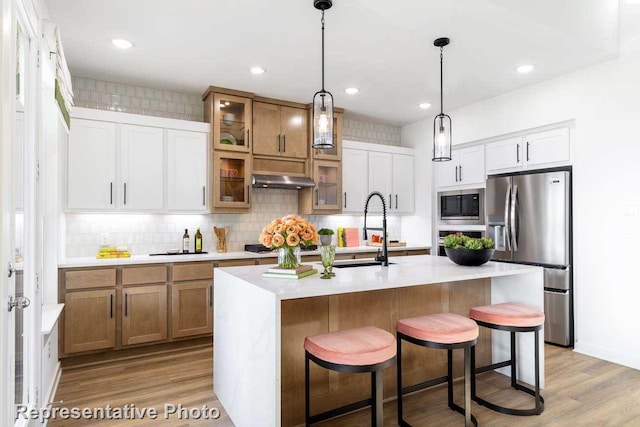 kitchen with a kitchen island with sink, white cabinetry, stainless steel appliances, and light wood-type flooring