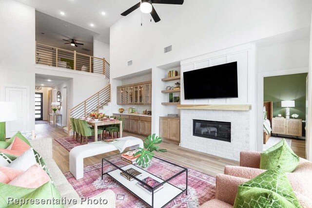 living room with ceiling fan, a towering ceiling, and light hardwood / wood-style flooring