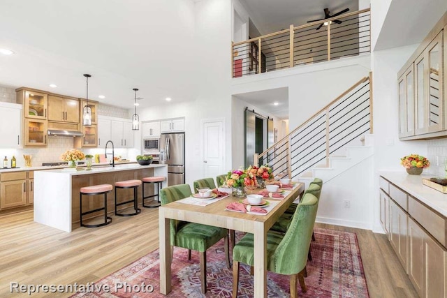 dining area with sink, light hardwood / wood-style flooring, ceiling fan, and a high ceiling