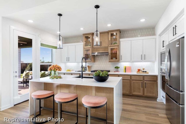 kitchen with stainless steel appliances, white cabinetry, sink, and a center island with sink