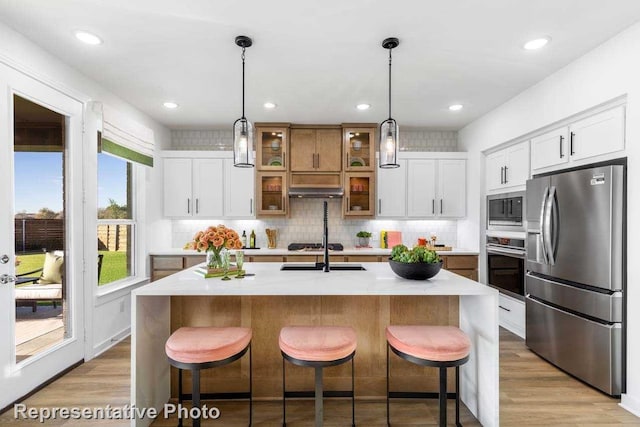 kitchen with a breakfast bar, appliances with stainless steel finishes, white cabinetry, a center island with sink, and decorative light fixtures