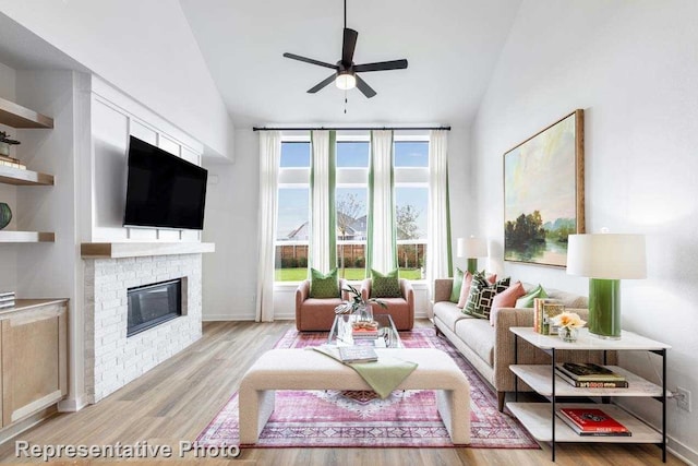 living room featuring lofted ceiling, a fireplace, ceiling fan, and light wood-type flooring