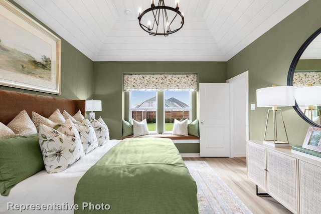 bedroom featuring vaulted ceiling, light hardwood / wood-style floors, and a notable chandelier