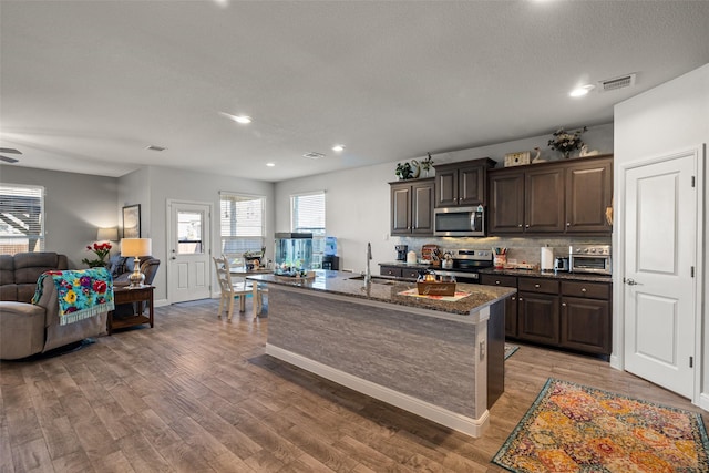 kitchen featuring appliances with stainless steel finishes, backsplash, dark brown cabinets, sink, and an island with sink