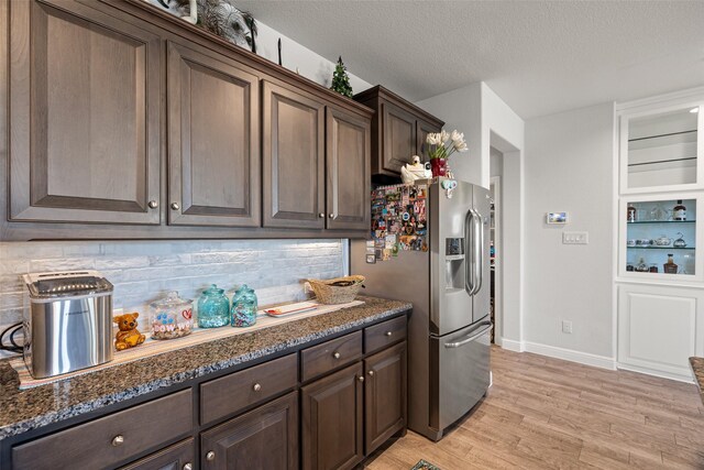 kitchen featuring backsplash, dark brown cabinets, dark stone countertops, and stainless steel refrigerator with ice dispenser