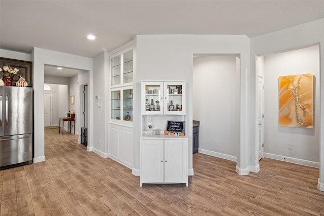 kitchen with stainless steel fridge, built in shelves, white cabinets, and light hardwood / wood-style flooring