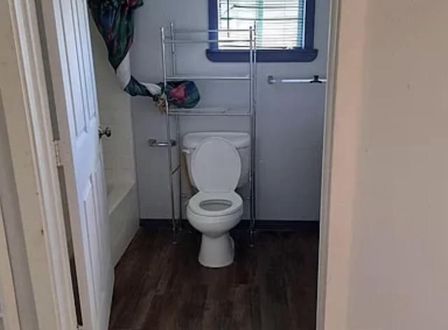 bathroom with wood-type flooring, a tub to relax in, and toilet