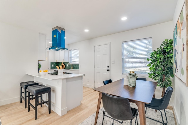 kitchen featuring white cabinets, light hardwood / wood-style flooring, tasteful backsplash, kitchen peninsula, and island exhaust hood