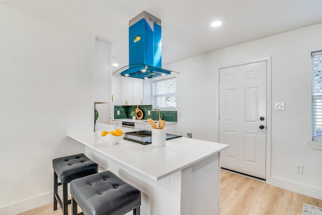 kitchen with a kitchen breakfast bar, kitchen peninsula, island range hood, and white cabinets