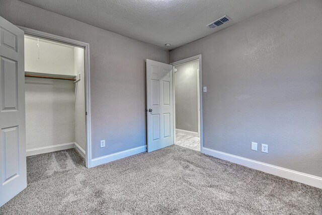 unfurnished bedroom with light carpet, a textured ceiling, and a closet