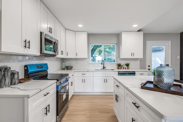 kitchen with white cabinets, sink, light stone countertops, light hardwood / wood-style floors, and stainless steel appliances