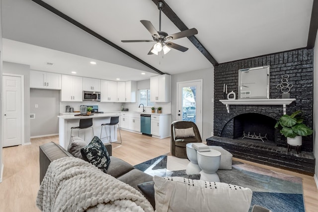 living room featuring ceiling fan, sink, a brick fireplace, vaulted ceiling with beams, and light hardwood / wood-style floors