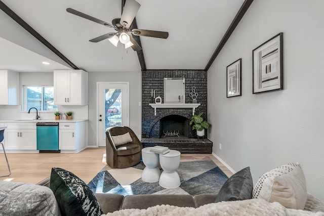 living room featuring sink, vaulted ceiling, ceiling fan, a fireplace, and light hardwood / wood-style floors