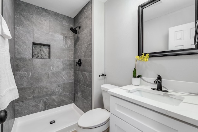 bathroom with tiled shower, vanity, and toilet