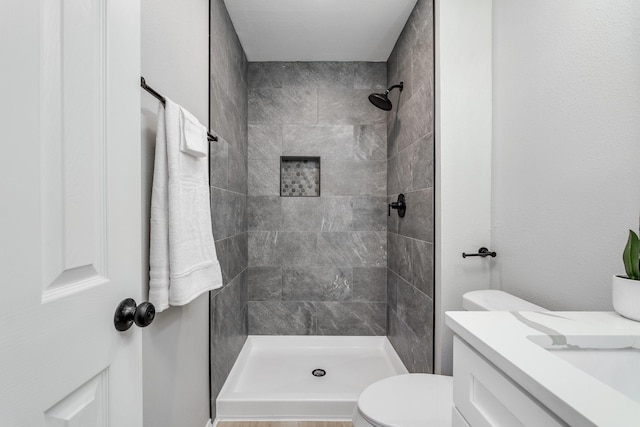 bathroom featuring a tile shower, vanity, and toilet