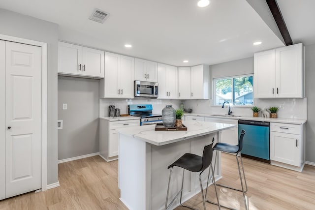 kitchen featuring beam ceiling, white cabinetry, a center island, sink, and appliances with stainless steel finishes