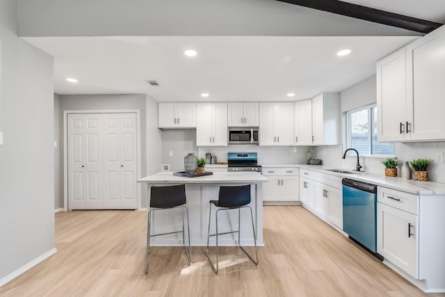 kitchen featuring a center island, sink, appliances with stainless steel finishes, white cabinets, and light wood-type flooring