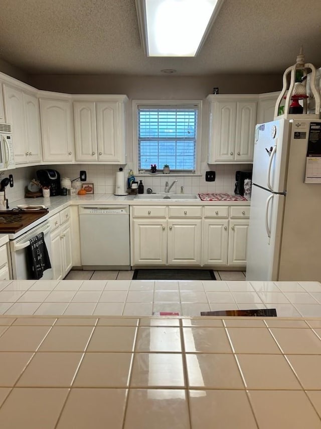 kitchen featuring tile countertops, white cabinetry, white appliances, and decorative backsplash