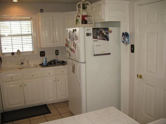 kitchen with white cabinetry, sink, backsplash, white refrigerator, and tile counters