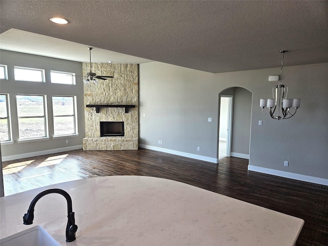 unfurnished living room with a fireplace, a textured ceiling, dark hardwood / wood-style flooring, and ceiling fan with notable chandelier