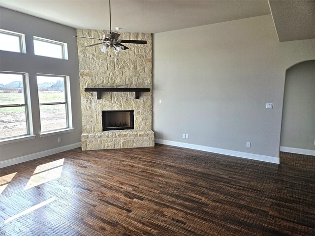 unfurnished living room featuring a stone fireplace, ceiling fan, dark hardwood / wood-style flooring, and a towering ceiling