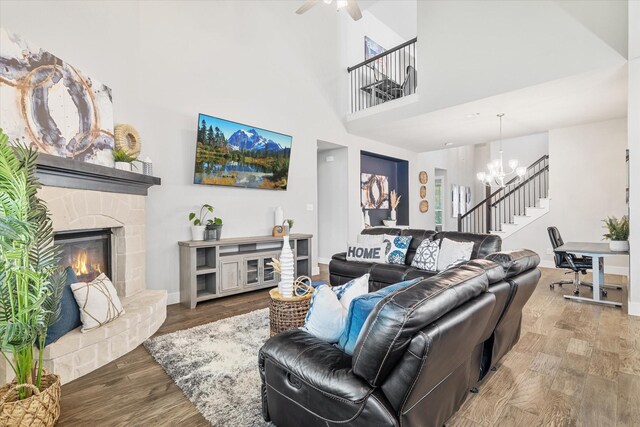 living room featuring hardwood / wood-style floors, a stone fireplace, ceiling fan with notable chandelier, and a towering ceiling