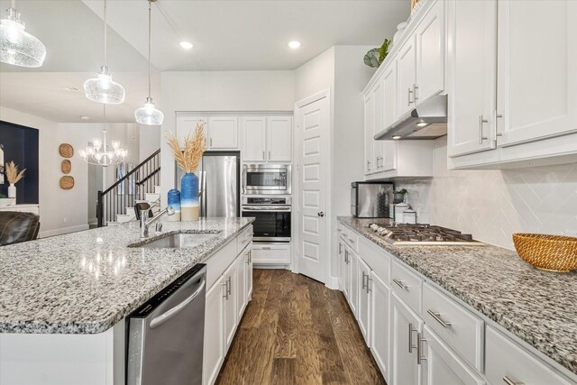 kitchen featuring sink, decorative light fixtures, appliances with stainless steel finishes, a kitchen island with sink, and white cabinets