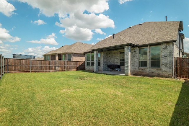 rear view of property featuring brick siding, roof with shingles, a fenced backyard, a yard, and a patio