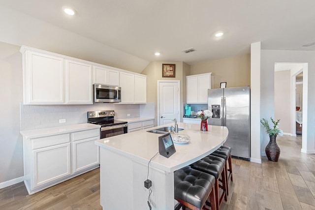 kitchen with stainless steel appliances, an island with sink, visible vents, and light wood finished floors