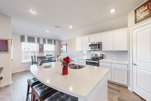 kitchen with white cabinets, stainless steel appliances, a center island with sink, and sink