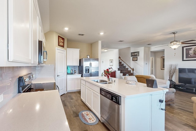 kitchen with white cabinetry, wood finished floors, a sink, stainless steel appliances, and open floor plan