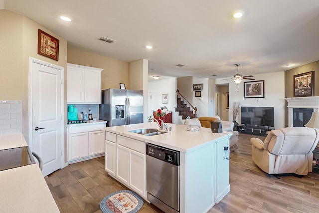 kitchen with white cabinetry, sink, stainless steel appliances, backsplash, and a center island with sink