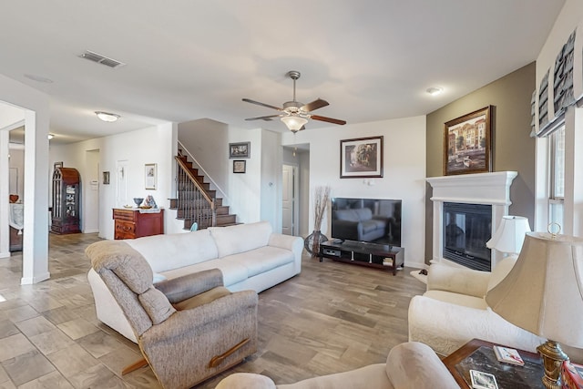 living area featuring visible vents, baseboards, a ceiling fan, stairway, and a glass covered fireplace