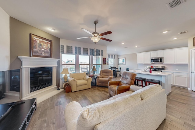 living room featuring light wood-type flooring, ceiling fan, and sink