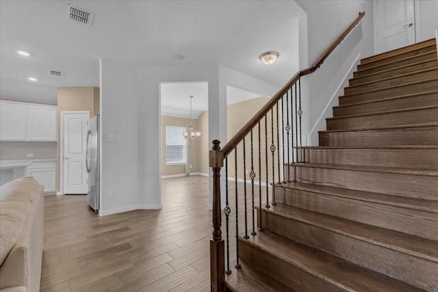 stairway featuring visible vents, baseboards, a chandelier, and wood finished floors