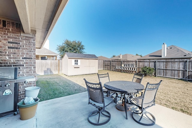 view of patio / terrace featuring outdoor dining space, a fenced backyard, a storage unit, and an outbuilding