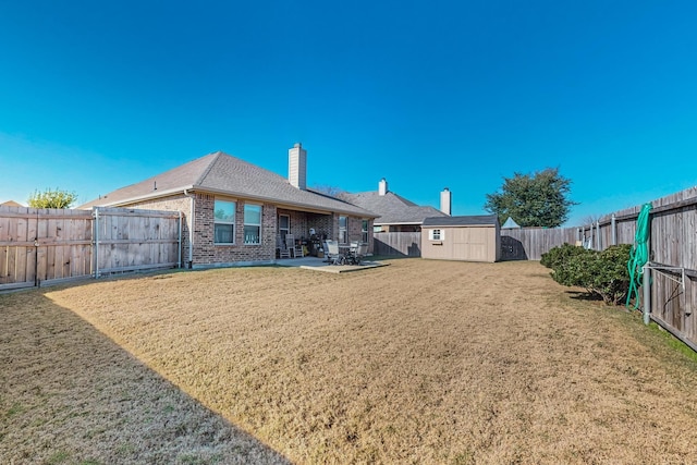 back of property featuring an outbuilding, a lawn, a chimney, a fenced backyard, and brick siding