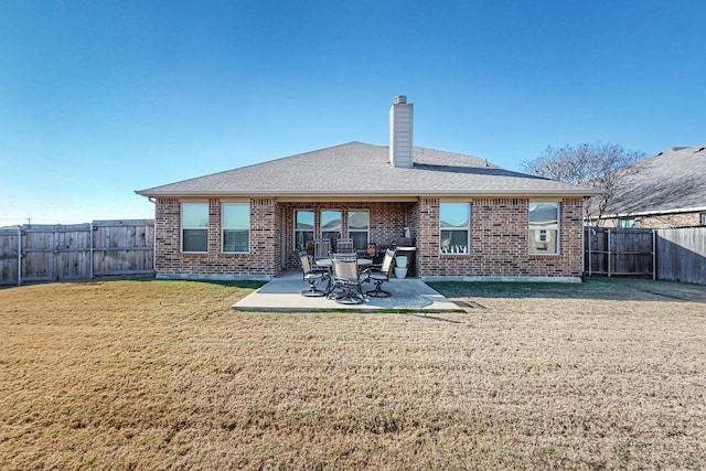rear view of house with a yard, a patio area, a chimney, a fenced backyard, and brick siding