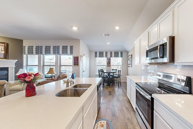 kitchen featuring light wood-type flooring, appliances with stainless steel finishes, a sink, light countertops, and open floor plan