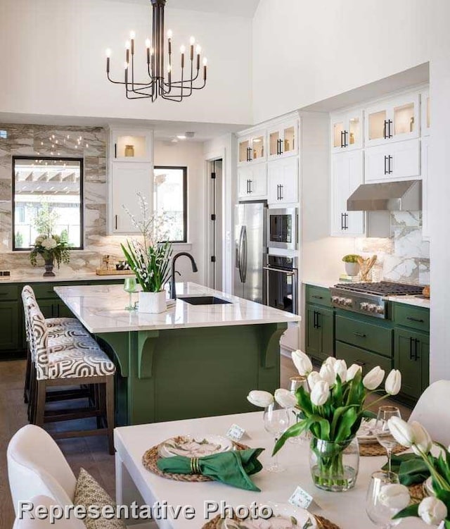 kitchen with appliances with stainless steel finishes, decorative light fixtures, white cabinetry, sink, and a kitchen island with sink