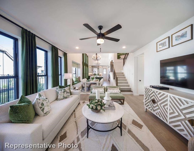 living room featuring ceiling fan with notable chandelier and light hardwood / wood-style flooring