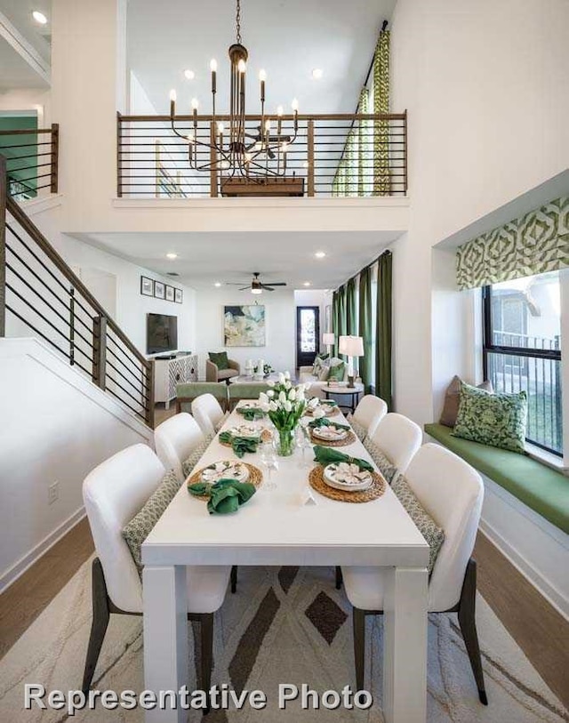 dining area featuring a towering ceiling, a wealth of natural light, ceiling fan with notable chandelier, and light wood-type flooring