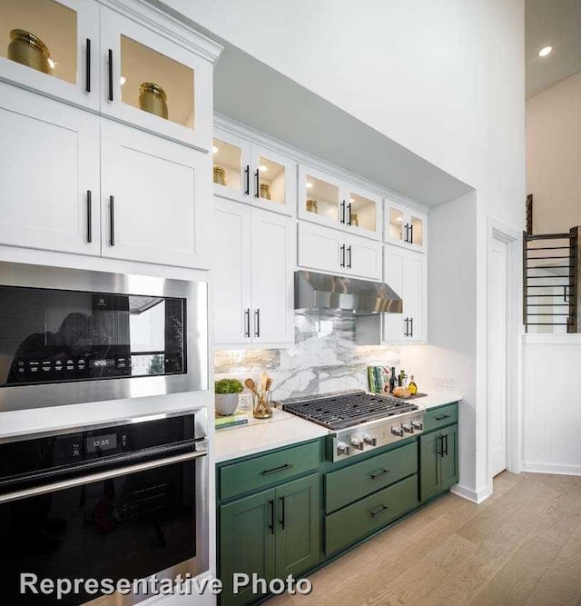 kitchen featuring white cabinetry, light wood-type flooring, green cabinets, stainless steel appliances, and backsplash