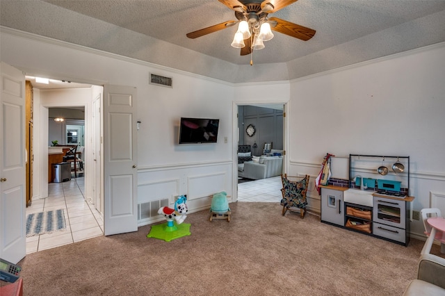 playroom with ceiling fan, light colored carpet, a raised ceiling, and a textured ceiling