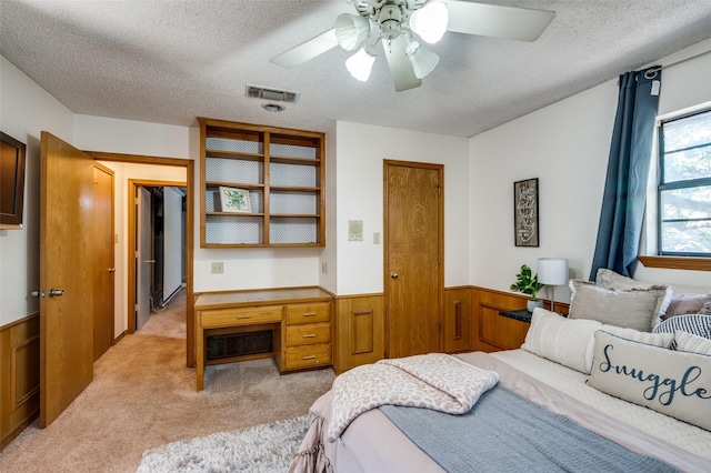 carpeted bedroom featuring ceiling fan, built in desk, a textured ceiling, and wood walls